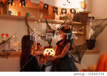 Halloween Joy. Mother and daughter sharing a glowing pumpkin moment. Halloween Joy. Mother and daughter sharing a glowing pumpkin moment. 133415714