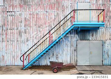 Wall of an old industrial building with stairs and a wheelbarrow. Wall of an old industrial building with stairs and a wheelbarrow. 133415831