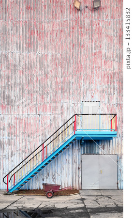 Wall of an old industrial building with stairs and a wheelbarrow. 133415832