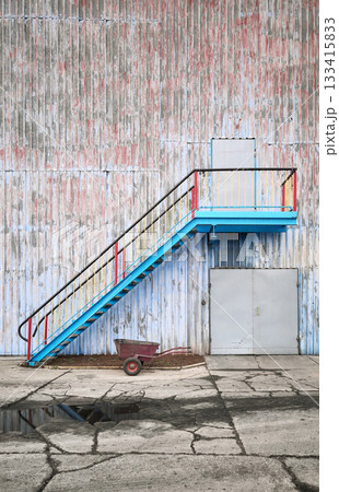 Wall of an old industrial building with stairs and a wheelbarrow. 133415833