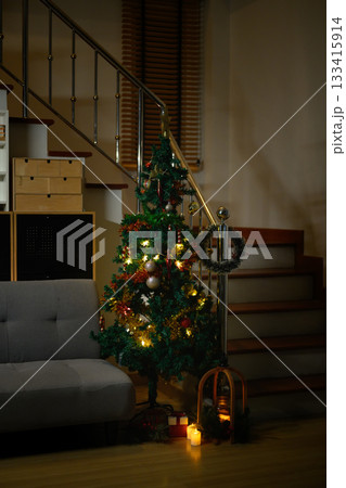 Cozy Christmas Tree with Glowing Lights in living room Interior with grey Sofa and Staircase Beside 133415914