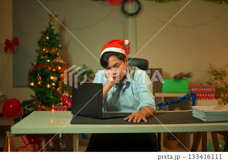 Bored, Christmas hat and portrait of a tired man in the office with a laptop, exhausted and young businessman with xmas decorations in the modern workplace. 133416111