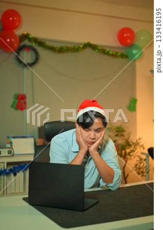 Bored, Christmas hat and portrait of a tired man in the office with a laptop, exhausted and young businessman with xmas decorations in the modern workplace. Bored, Christmas hat and portrait of a tired man in the office with a laptop, exhausted and young businessman with xmas decorations in the modern workplace. 133416195