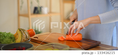 Closeup of young female hands chopping fresh orange carrot on board while in modern kitchen 133416215