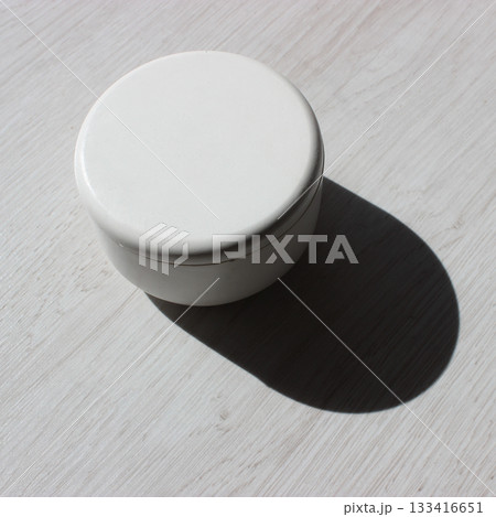 A deep shadow cast by a craft round caddy box standing on a wooden table square stock photo A deep shadow cast by a craft round caddy box standing on a wooden table square stock photo 133416651