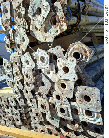 Metal construction supports are neatly stacked in an industrial yard. They show signs of wear and rust, indicating previous use. The scene captures the organized storage of construction materials. 133416687