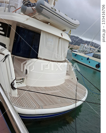 A luxurious yacht is securely moored at Denia's port in Spain. The setting features a calm water surface and gentle waves, with scenic coastal mountains in the background. A luxurious yacht is securely moored at Denia's port in Spain. The setting features a calm water surface and gentle waves, with scenic coastal mountains in the background. 133416706