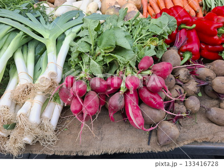 Vibrant eco bio farm vegetables are arranged beautifully at a market. Shoppers admire the colorful selection of radishes, leeks, and peppers under bright morning light. Vibrant eco bio farm vegetables are arranged beautifully at a market. Shoppers admire the colorful selection of radishes, leeks, and peppers under bright morning light. 133416728