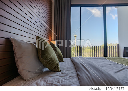 A bed with white sheets and green pillows sits against a wooden panel wall, with two wall lamps and small side tables creating a simple layout. 133417371