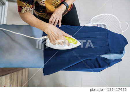 Senior citizens ironing student skirt and clothing in a house. 133417455