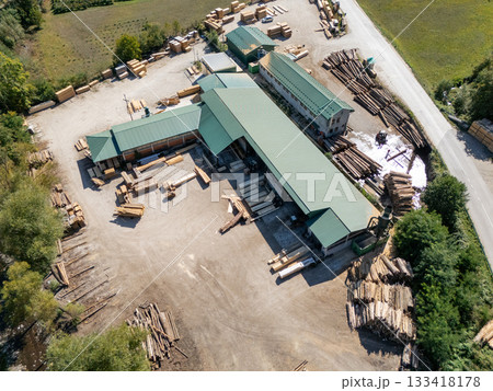 Aerial view of a sawmill factory in the mountains surrounded by dense forest, with stacks of processed lumber and timber 133418178