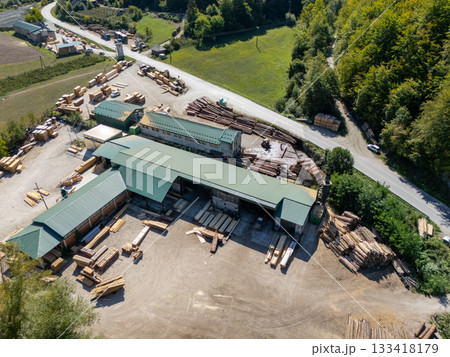 Aerial view of a sawmill factory in the mountains surrounded by dense forest, with stacks of processed lumber and timber 133418179