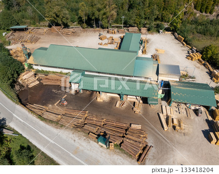 Aerial view of a sawmill factory in the mountains surrounded by dense forest, with stacks of processed lumber and timber 133418204