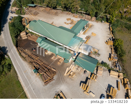 Aerial view of a sawmill factory in the mountains surrounded by dense forest, with stacks of processed lumber and timber Aerial view of a sawmill factory in the mountains surrounded by dense forest, with stacks of processed lumber and timber 133418210