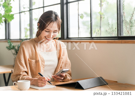 カフェでタブレットとスマホを使いメモを取る若いアジア人女性 カフェでタブレットとスマホを使いメモを取る若いアジア人女性 133421081
