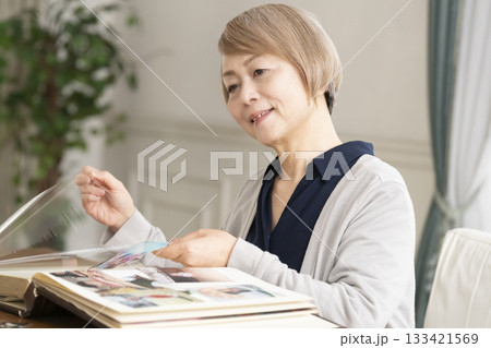 孫や子供の写真をアルバムに入れるシニア女性 孫や子供の写真をアルバムに入れるシニア女性 133421569