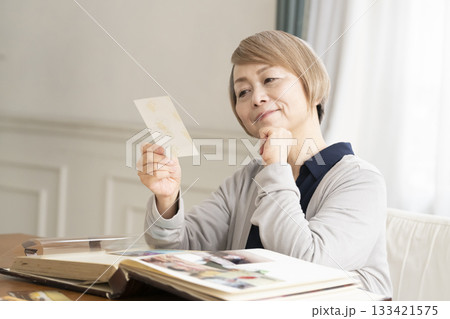 孫や子供の写真をアルバムに入れるシニア女性 孫や子供の写真をアルバムに入れるシニア女性 133421575