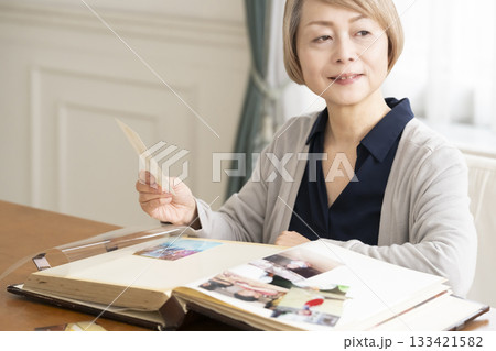 孫や子供の写真をアルバムに入れるシニア女性 133421582