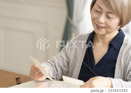 孫や子供の写真をアルバムに入れるシニア女性 133421583