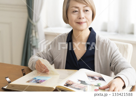 孫や子供の写真をアルバムに入れるシニア女性 133421588