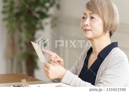 孫や子供の写真をアルバムに入れるシニア女性 孫や子供の写真をアルバムに入れるシニア女性 133421590