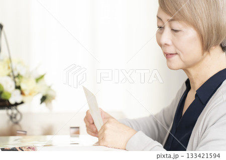 孫や子供の写真をアルバムに入れるシニア女性 133421594