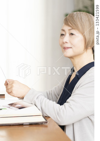 孫や子供の写真をアルバムに入れるシニア女性 133421599