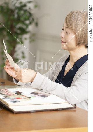 孫や子供の写真をアルバムに入れるシニア女性 孫や子供の写真をアルバムに入れるシニア女性 133421600
