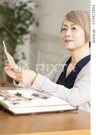 孫や子供の写真をアルバムに入れるシニア女性 孫や子供の写真をアルバムに入れるシニア女性 133421601