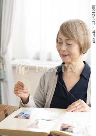 孫や子供の写真をアルバムに入れるシニア女性 133421609