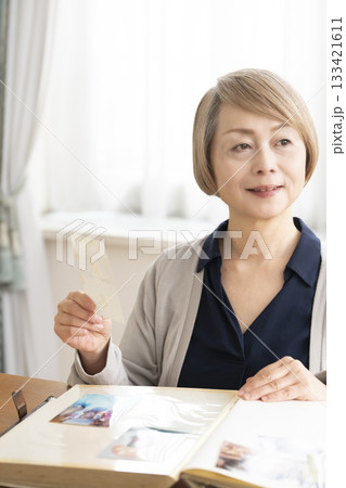 孫や子供の写真をアルバムに入れるシニア女性 孫や子供の写真をアルバムに入れるシニア女性 133421611