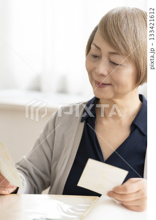 孫や子供の写真をアルバムに入れるシニア女性 孫や子供の写真をアルバムに入れるシニア女性 133421612