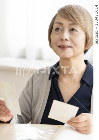 孫や子供の写真をアルバムに入れるシニア女性 孫や子供の写真をアルバムに入れるシニア女性 133421614