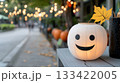 Smiling round paper lantern gently glows on a wooden surface, set for the Ghost Festival. Soft golden string lights and autumn pumpkins create a festive and mysterious outdoor evening scene. 133422005