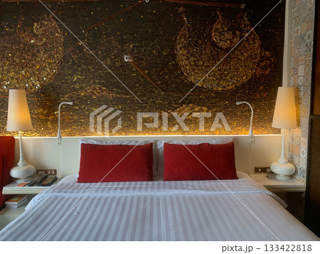 Luxury hotel bedroom with red pillows, lamps, and a decorative wall feature	 133422818