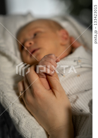 A mother cradles her babys tiny hand, both feeling warmth and love while sharing a tender moment in a softly lit environment. 133423015