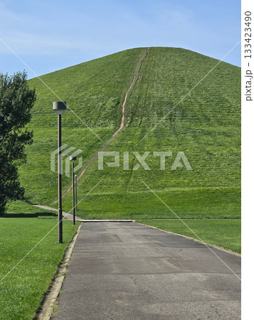 A paved path leads toward a large grassy hill with a walking trail, creating a sense of journey and exploration 133423490