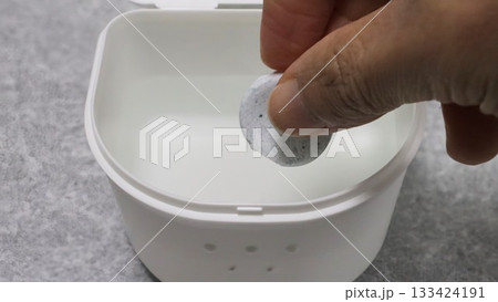 マウスピース用の容器に洗浄剤を入れる人物 133424191