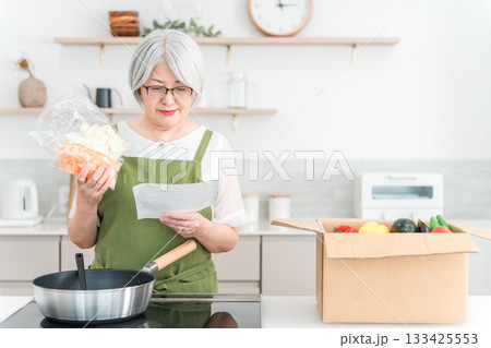 家のキッチンでミールキット,料理キットで料理をするシニア・高齢者女性（笑顔） 133425553