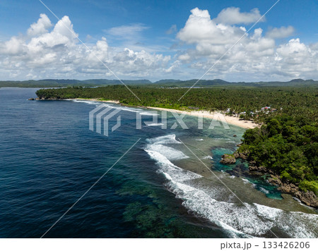 Shoreline with sandy beach, rocky edges, and tropical forest meeting the ocean waves. Siargao, Philippines. Magpupungko Tidal Pool. 133426206