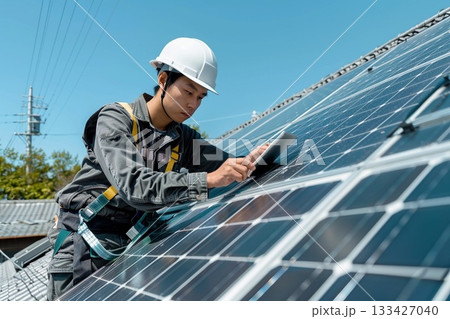青空の下でタブレットを使い太陽光発電ソーラーパネルの点検を行う作業員 133427040