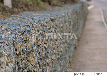 A stone fence secured with metal mesh along a pedestrian sidewalk. A stone fence secured with metal mesh along a pedestrian sidewalk. 133428549