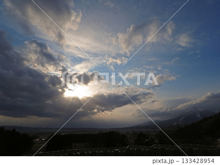 雲の切れ間から磐梯山の裾野に輝く太陽。放射状の光が地上差し込み、青空に印象的で綺麗だ。 133428954