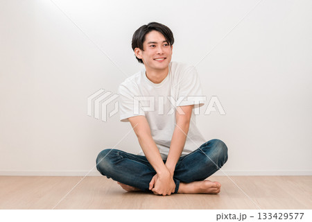 リビングにあぐらで座る笑顔の若いアジア人男性（メンズビューティー） 133429577