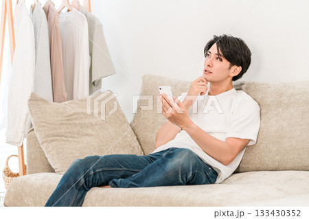 リビングのソファーでスマホを見ながら考え事をする若いアジア人男性 リビングのソファーでスマホを見ながら考え事をする若いアジア人男性 133430352