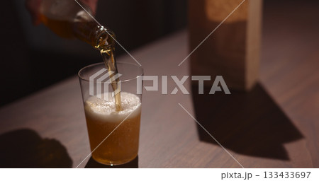 Man pour amber color fizzy drink in tumbler glass with bag of potato chips on background 133433697