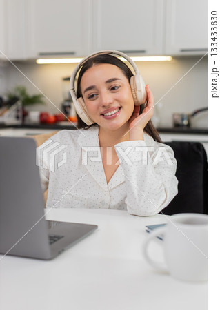 Young woman types on laptop in headphones smiles nods to rhythm music plays typing client email live Young woman types on laptop in headphones smiles nods to rhythm music plays typing client email live 133433830
