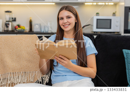 Young woman reads book enjoys leisure time smiles calm comfort simple weekend mood indoor rest joy Young woman reads book enjoys leisure time smiles calm comfort simple weekend mood indoor rest joy 133433831