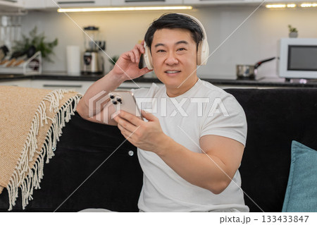 Asian man with wireless headphones enjoys playlist relaxes closes eyes rocks gently and smiles calm Asian man with wireless headphones enjoys playlist relaxes closes eyes rocks gently and smiles calm 133433847