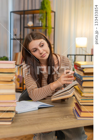 Young woman surrounded by books writes notes from textbook feels exhausted yet continues heavy study 133433854